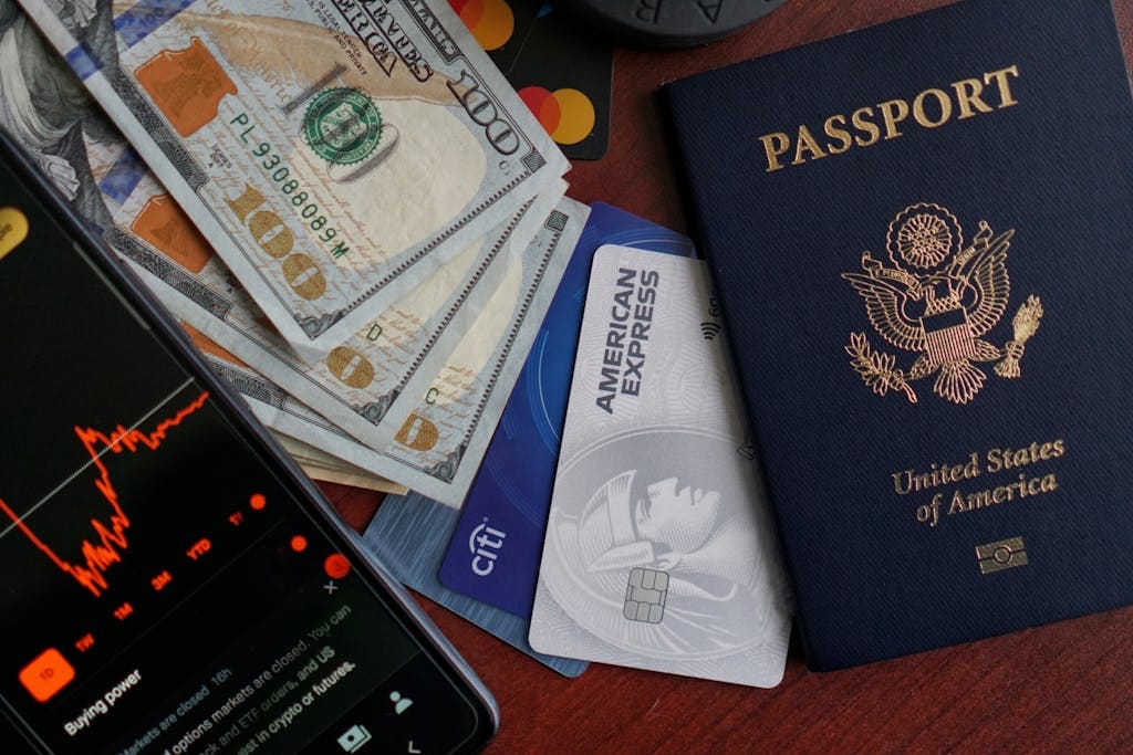 Top view of US passport, credit cards, cash, and phone showing financial graph, ideal for travel themes.