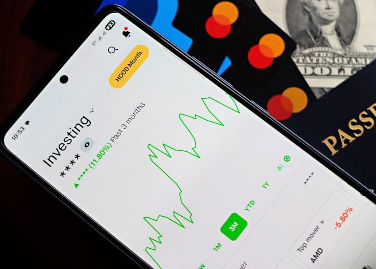 A smartphone showing an investment app with green growth indicators, surrounded by credit cards, US dollars, and a passport.