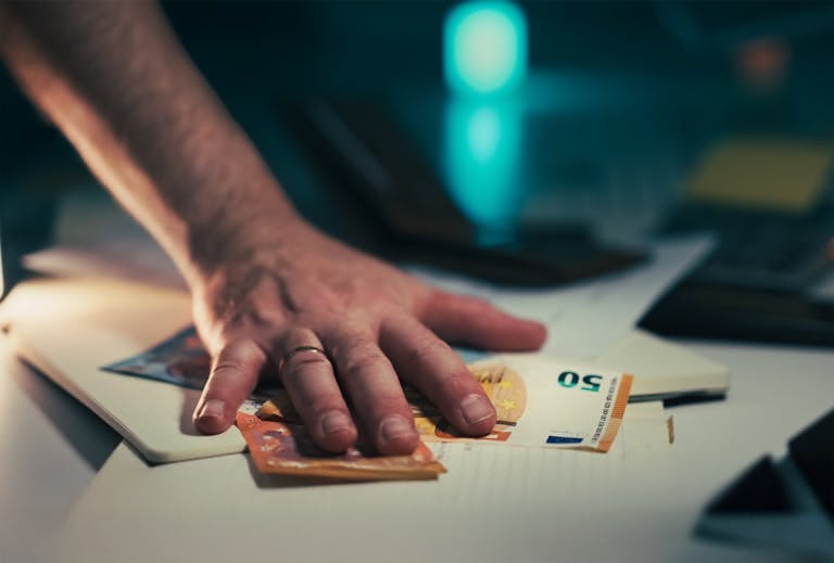 Close-up of a hand grabbing euro bills from a cluttered desk, symbolizing finance or financial crisis.