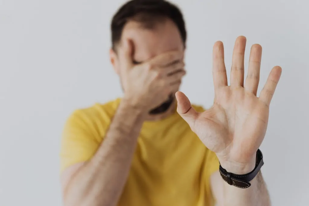 Close-up of a man covering his face and showing a stop gesture with his hand.