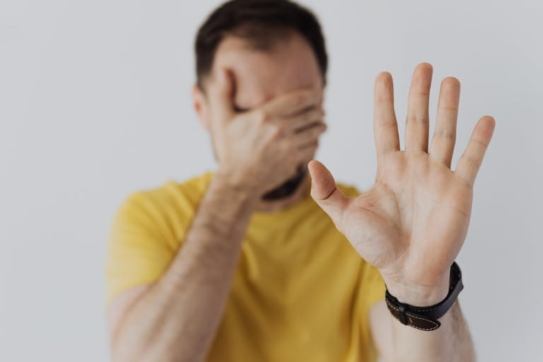 Close-up of a man covering his face and showing a stop gesture with his hand.