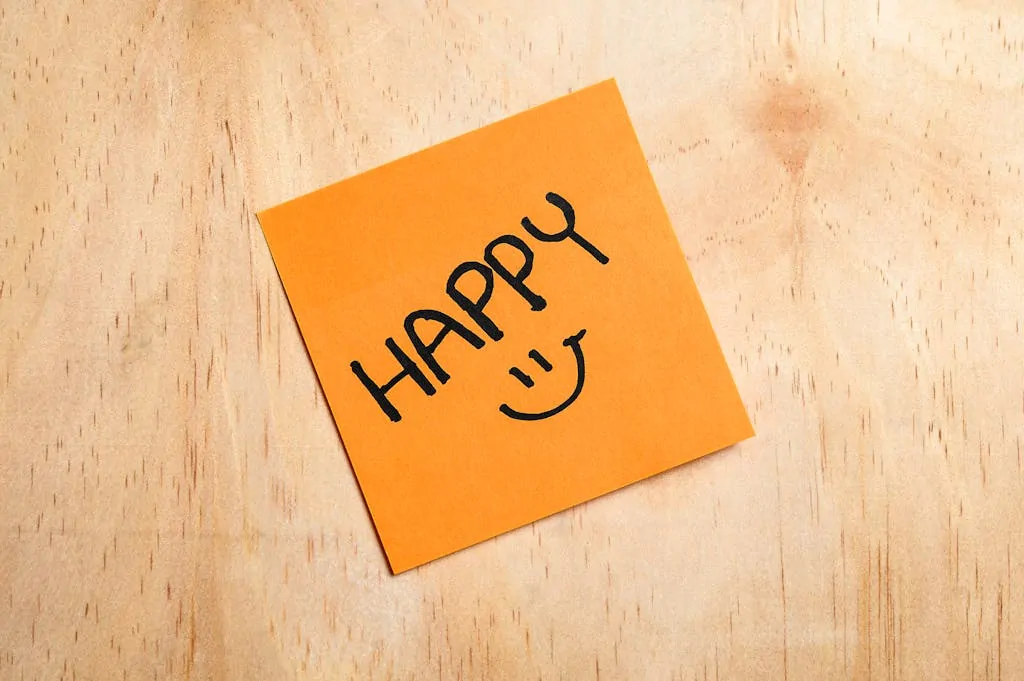 Orange sticky note on wood with the word 'HAPPY' and a smiley face.