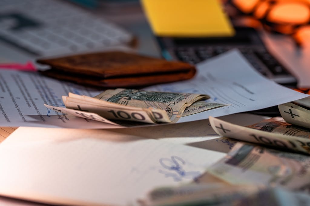 Zloty banknotes and financial paperwork scattered on a desk, representing budgeting and finance.