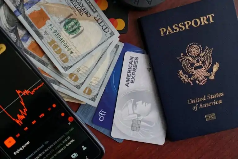 Top view of US passport, credit cards, cash, and phone showing financial graph, ideal for travel themes.