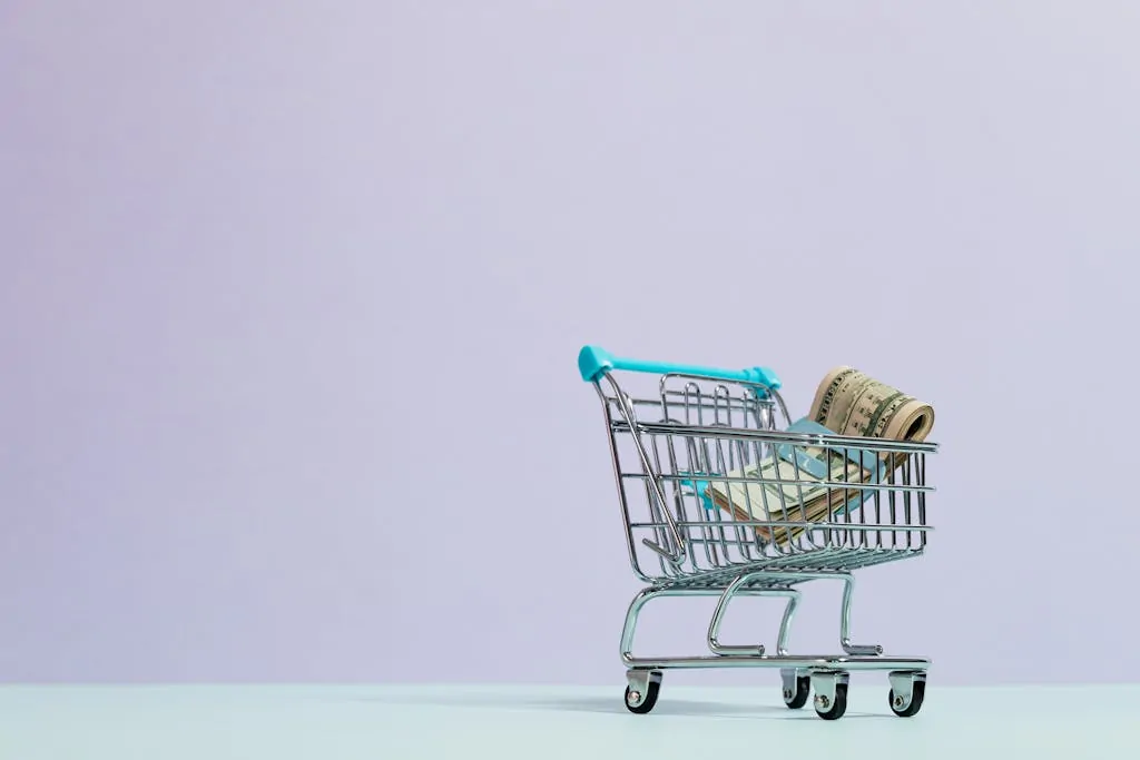 12 Easy Ways to Save Money on Groceries 1 A close-up of a mini shopping cart with rolled cash on a pastel background. Ideal for finance and ecommerce themes.