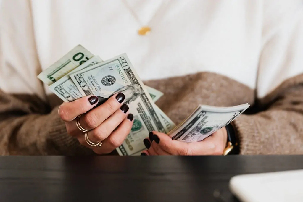 10+ Money Saving Tips Every Mom Needs 1 Close-up of hands counting US dollar bills, depicting finance and money handling.