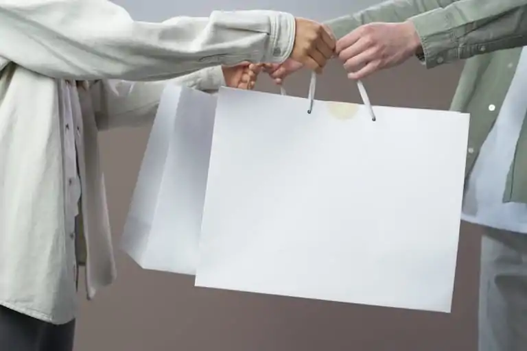 Midsection view of two people exchanging white shopping bags indoors.