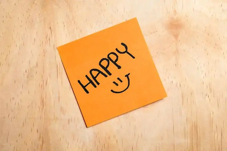 12 Easy Ways to Live Cheap (and Happy) 6 Orange sticky note on wood with the word 'HAPPY' and a smiley face.