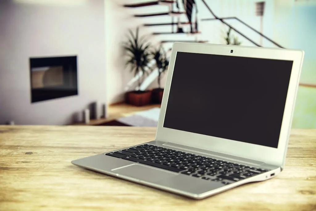 14 Ways to Get a Free or Cheap Laptop 1 Sleek laptop on a wooden desk with blurred contemporary home interior in the background.