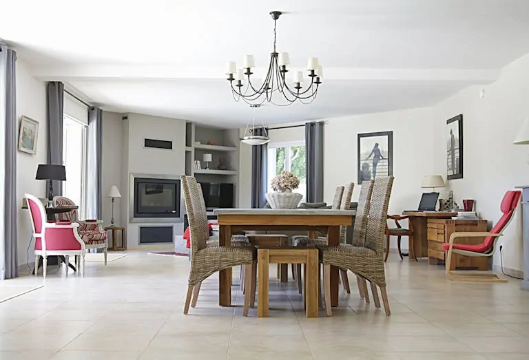 Spacious dining room with a chic chandelier, wicker chairs, wooden table, and cozy fireplace.