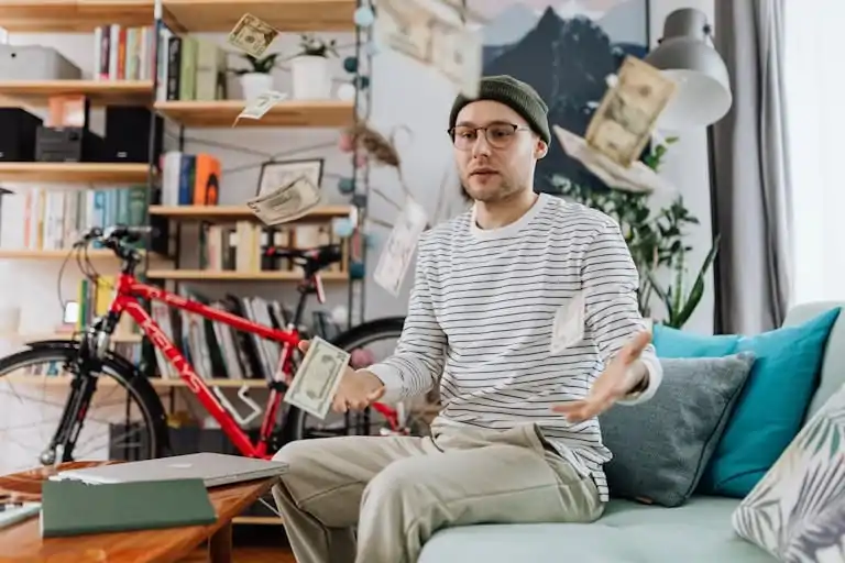 Young man tossing money in a cozy room, showcasing indoor leisure and wealth.
