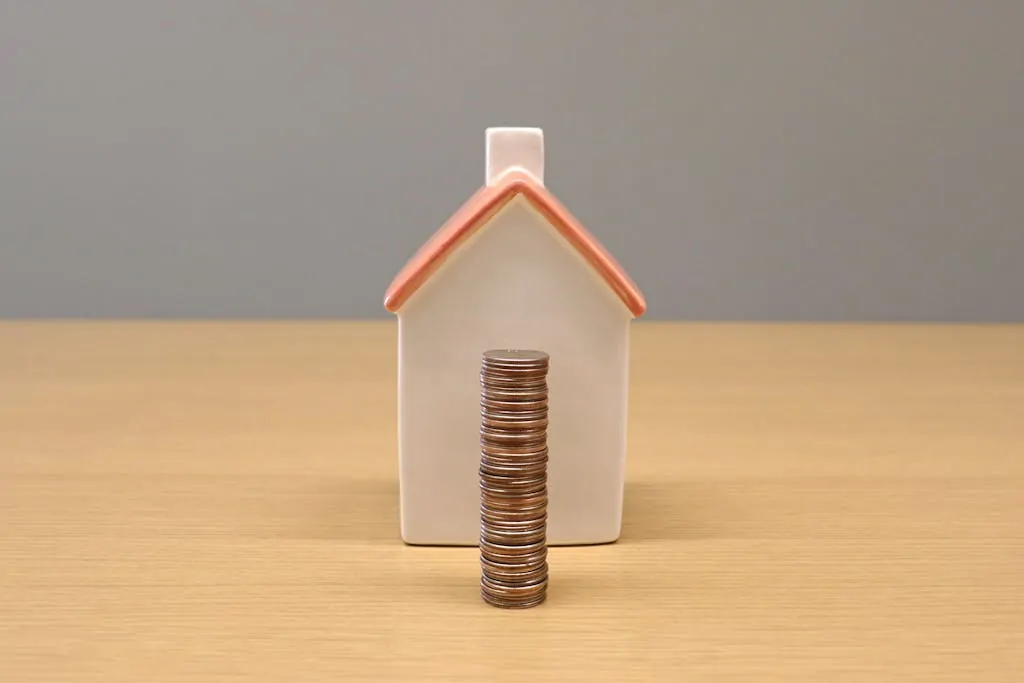 A conceptual still life image of stacked coins in front of a porcelain house, symbolizing savings and investment.