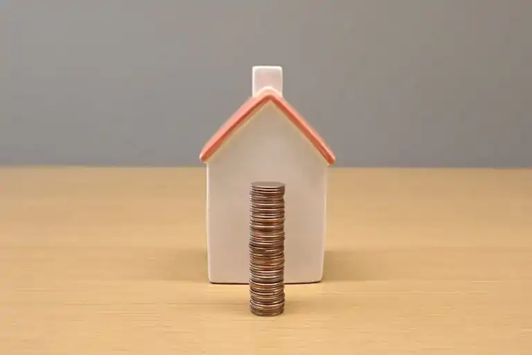 A conceptual still life image of stacked coins in front of a porcelain house, symbolizing savings and investment.