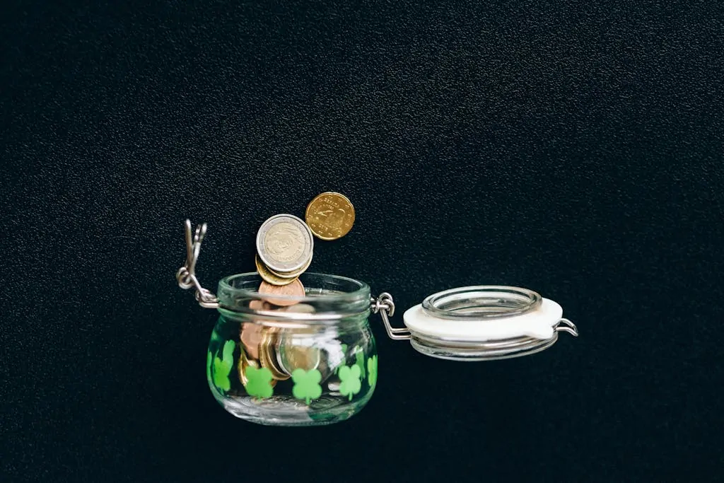 10 Ways to Beat Fear and Start Saving Money 1 Glass jar with coins falling into it on a black background, symbolizing savings.