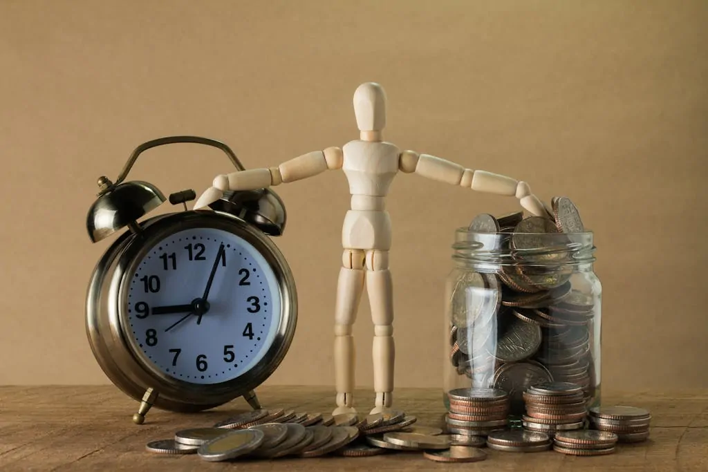 7 Savings Goals Worth Your Time and Money 1 Wooden mannequin holding an alarm clock and a jar full of coins, symbolizing time and money.